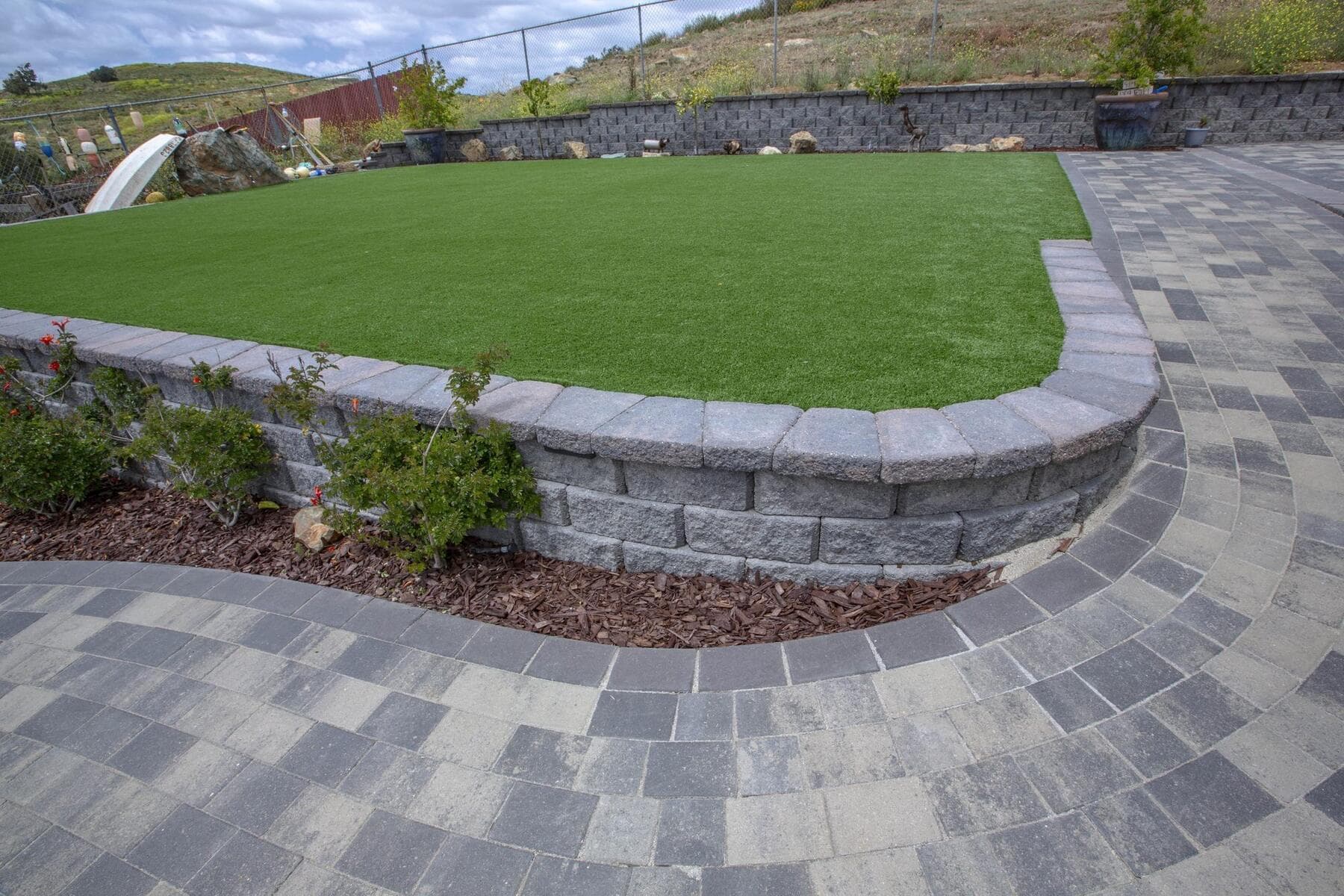 Curved paver patio wrapping a turf lawn and block retaining wall in Spring Valley