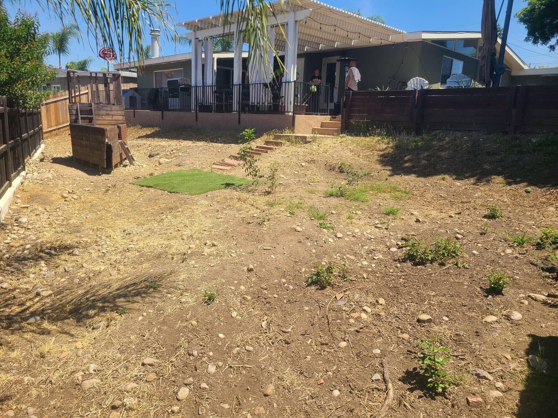 Dirt slope and leftover turf patch in the La Mesa backyard before the wall, turf, and pavers