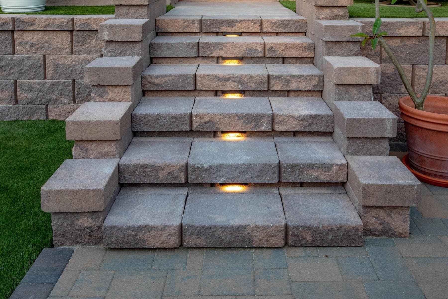 Lit block stairs between the turf lawn and paver patio