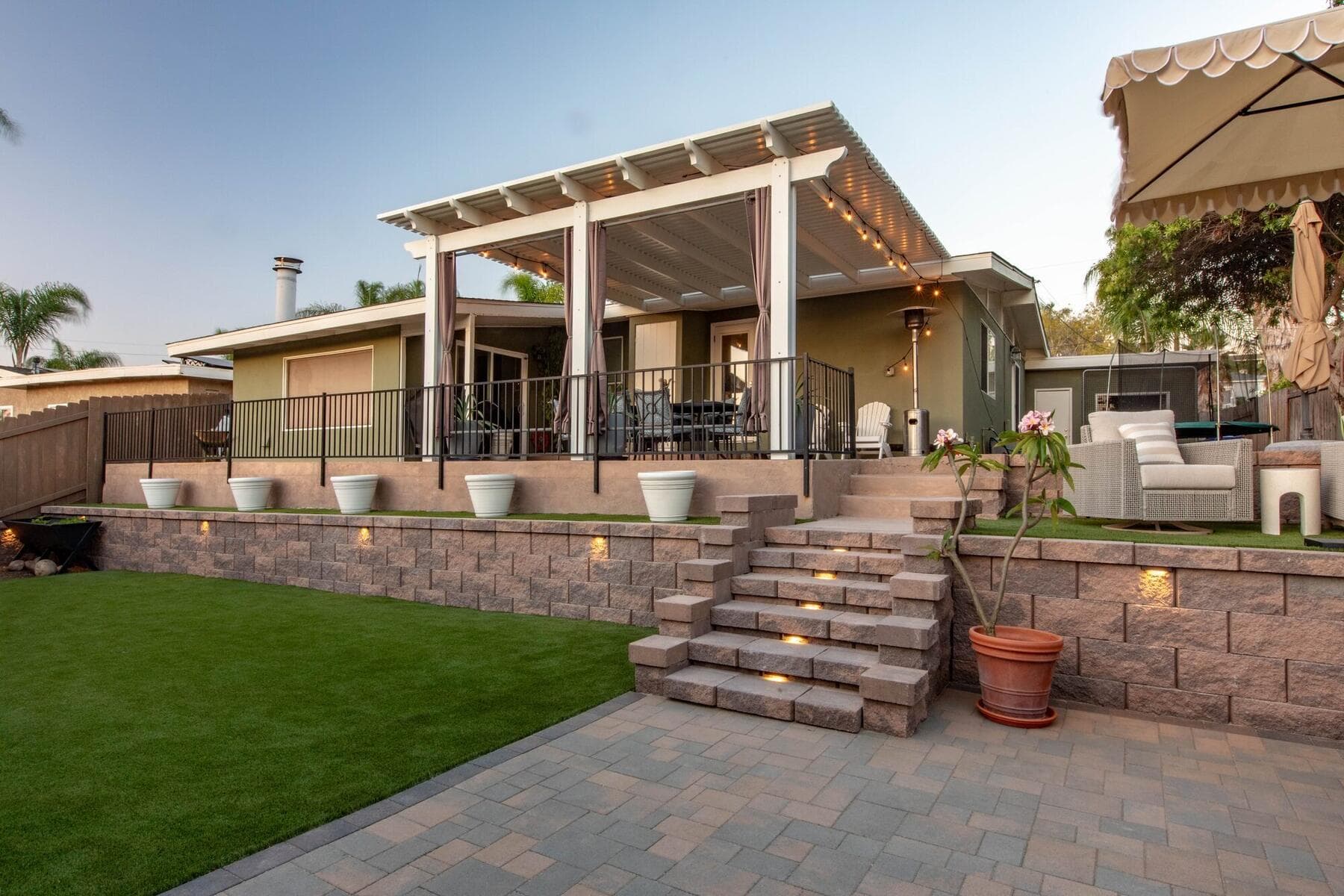 Block retaining wall, turf lawn, paver patio, and lit stairs in a La Mesa backyard