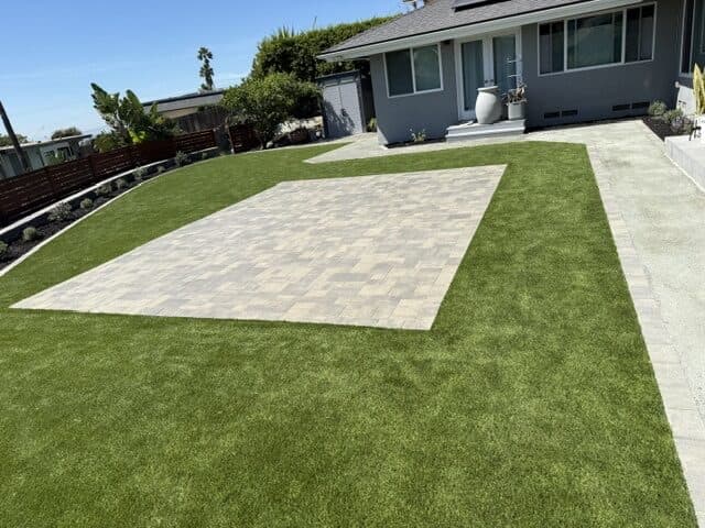 Paver patio set in turf beside a gray house, DG walk, and coastal planting