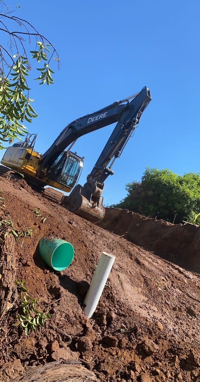 Deere excavator on a slope with drainage pipe in the cut